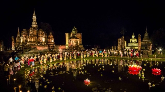 Rows of lit candles and floating krathong across Sukhothai Historical Park at night