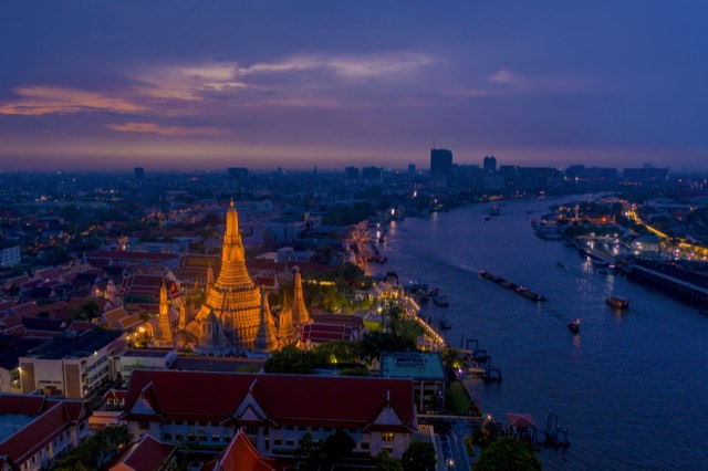 Wat Arun lit up at dusk beside the Chao Phraya river in Bangkok